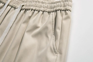 Detail view of elastic waistband with white drawstrings on beige cargo shorts