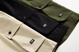 Detailed close-up of tactical cargo shorts showing side pockets with snap buttons and labels