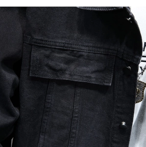 Dettaglio della giacca di jeans nera con tasca a busta e bottoni in metallo opaco nero
