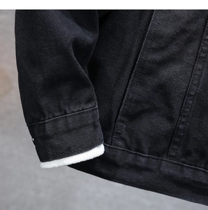 Dettaglio ravvicinato del polsino della giacca di jeans nera con coste bianche e tasca
