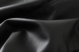 Macro detail of high-quality black PU leather texture with refined stitching on jacket