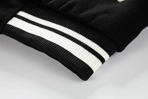 Detailed close-up of ribbed cuffs with white stripes on a black wool baseball jacket sleeve