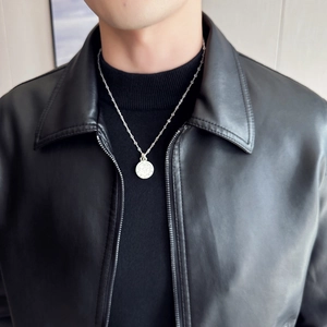 Close-up of silver coin pendant necklace with cross emblem on a black leather jacket
