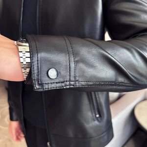 Detail of the sleeve cuff with double-stitched seams and metal snap button on black PU leather