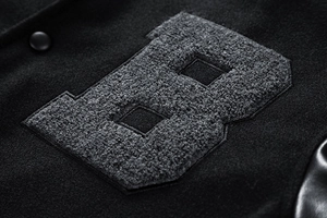 Detail of chenille embroidery B patch on black varsity jacket with leather texture
