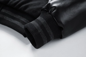 Detail of black leather sleeve and striped ribbed cuffs on the baseball jacket