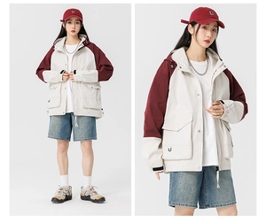Close-up of cream and burgundy outdoor hooded jacket with multi-pocket utility design