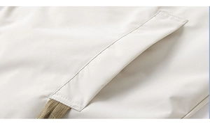 Detail of a beige jacket featuring high-quality stitching on a pocket and khaki drawstrings