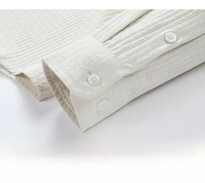 Macro detail of white long-sleeve shirt cuff featuring quilted grid texture and white buttons