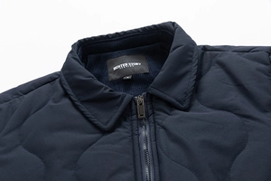 Detail of navy quilted jacket featuring corduroy collar, metal zipper, and brand neck label