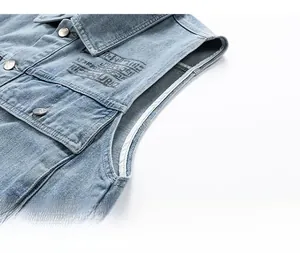 Close-up of light blue denim vest showing metal buttons and vintage letter prints