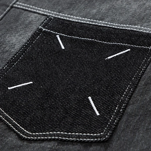 Détail d'une chemise en jean gris foncé montrant la broderie à quatre points sur la poche