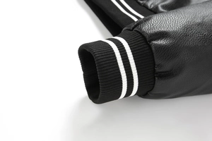 Detail of black PU leather jacket cuff with white striped ribbed knit texture and grain