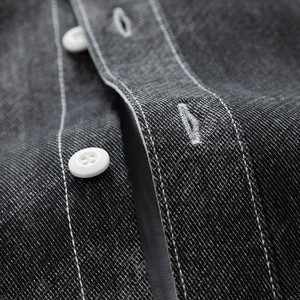 Gros plan d'une chemise en sergé gris foncé avec surpiqûres blanches et bouton rond