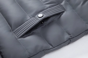 Macro shot of grey padded jacket pocket featuring neat quilting and a metallic snap button