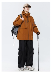 Veste de randonnée caramel imperméable et pantalon cargo noir avec bâtons de marche