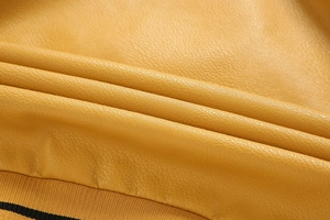 Close-up of yellow PU leather fabric with fine lychee texture and black striped ribbed cuffs