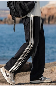 Dettaglio dei pantaloni sportivi con strisce laterali bianche e tipografia su tessuto nero