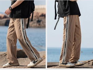 Dettaglio dei pantaloni outdoor kaki con strisce laterali bianche e nere e motivi testo