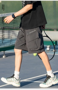 Detail view of dark grey cargo shorts with large utility pockets in a tennis court setting