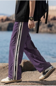 Dettaglio di pantaloni viola a gamba larga con fettuccia laterale su sfondo marino