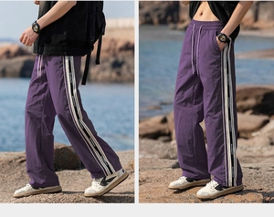 Dettaglio dei pantaloni viola a gamba larga con nastri laterali a righe e vita regolabile