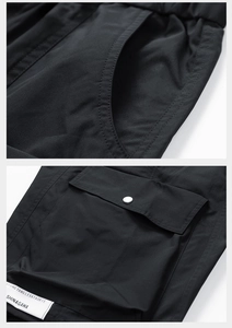 Detail of cargo pocket with silver snap button and brand label on black tech shorts