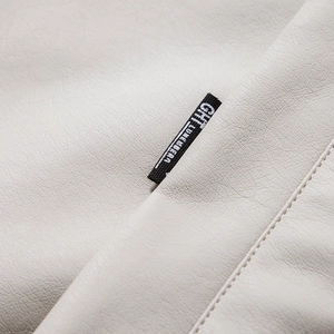 Macro shot of precise stitching and black brand label on white leather jacket fabric