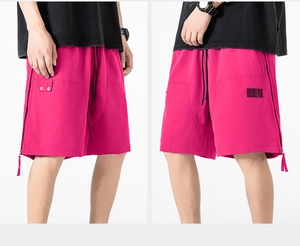 Detail view of pink loose-fit shorts featuring side straps and barcode fabric patch