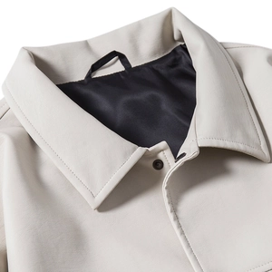 Detail of lapel collar and copper button on beige leather jacket with black lining