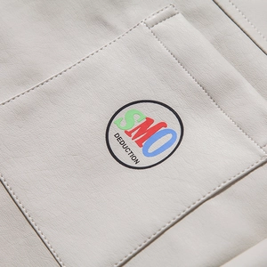 Detail of a creamy white leather jacket pocket with precise stitching and circular logo