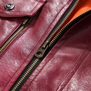 Detail of burgundy leather jacket with bronze zipper and bright orange inner lining