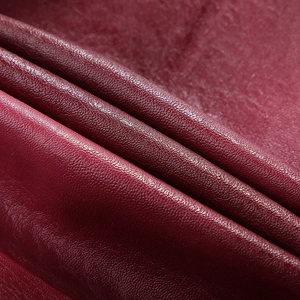 Detail shot of the burgundy PU leather texture with fine lychee grain on a motor jacket