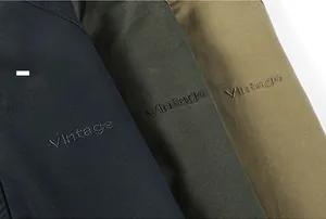 Detail of vintage embroidery on cotton twill jackets in navy, olive green, and khaki
