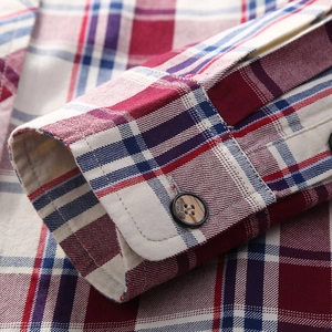 Close-up of red plaid cotton long sleeve shirt cuff with brown buttons and fine texture