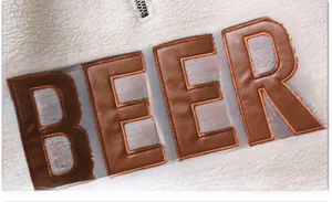 Détail du molleton sherpa blanc avec broderie de l'écusson BEER en similicuir marron