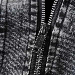 Close-up of a silver metal zipper on a grey acid wash denim jacket with a vintage finish