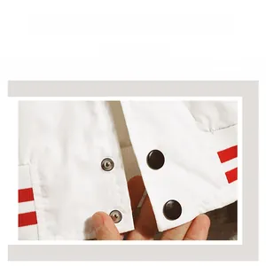Detail shot of white baseball jacket featuring red striped ribbed hem and snap buttons