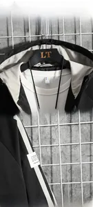 Detail view of black hooded jacket featuring contrast striped cuffs and letter patch
