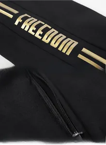 Detail of the golden FREEDOM print and hidden zipper pocket on a black sports tracksuit