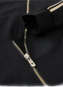 Detail view of black sportswear jacket showing golden stripes on cuffs and metal zipper puller