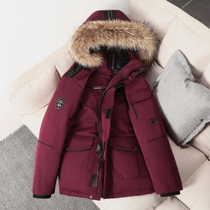 Parka d'hiver bordeaux avec grand col en fourrure et poches cargo sur canapé beige