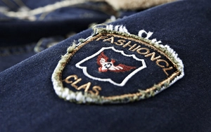 Detailed macro view of denim jacket showing shield embroidery and distressed raw edge finish