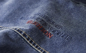 Detail of blue denim fabric with red and black fashion embroidery and orange stitching
