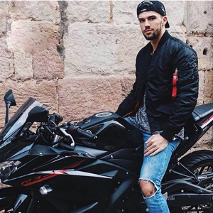 Classic black bomber jacket in shiny nylon with signature red flight tag on motorcycle