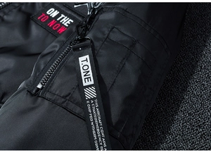 Dettaglio della giacca bomber in nylon nero con zip metallica e tasca sulla manica