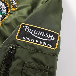 Gros plan sur la manche d'un blouson bomber vert foncé avec broderie et poche zippée