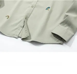 Detailed macro shot of pale green shirt hem featuring rainbow embroidery and buttons