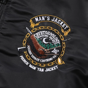 Gros plan sur l'écusson brodé d'une veste bomber noire avec motif de forêt et de croissant