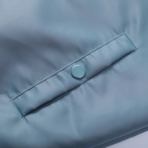 Detail of blue bomber jacket pocket featuring smooth nylon fabric and secure snap button